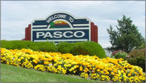 A sign that says welcome to pasco with flowers in the foreground.