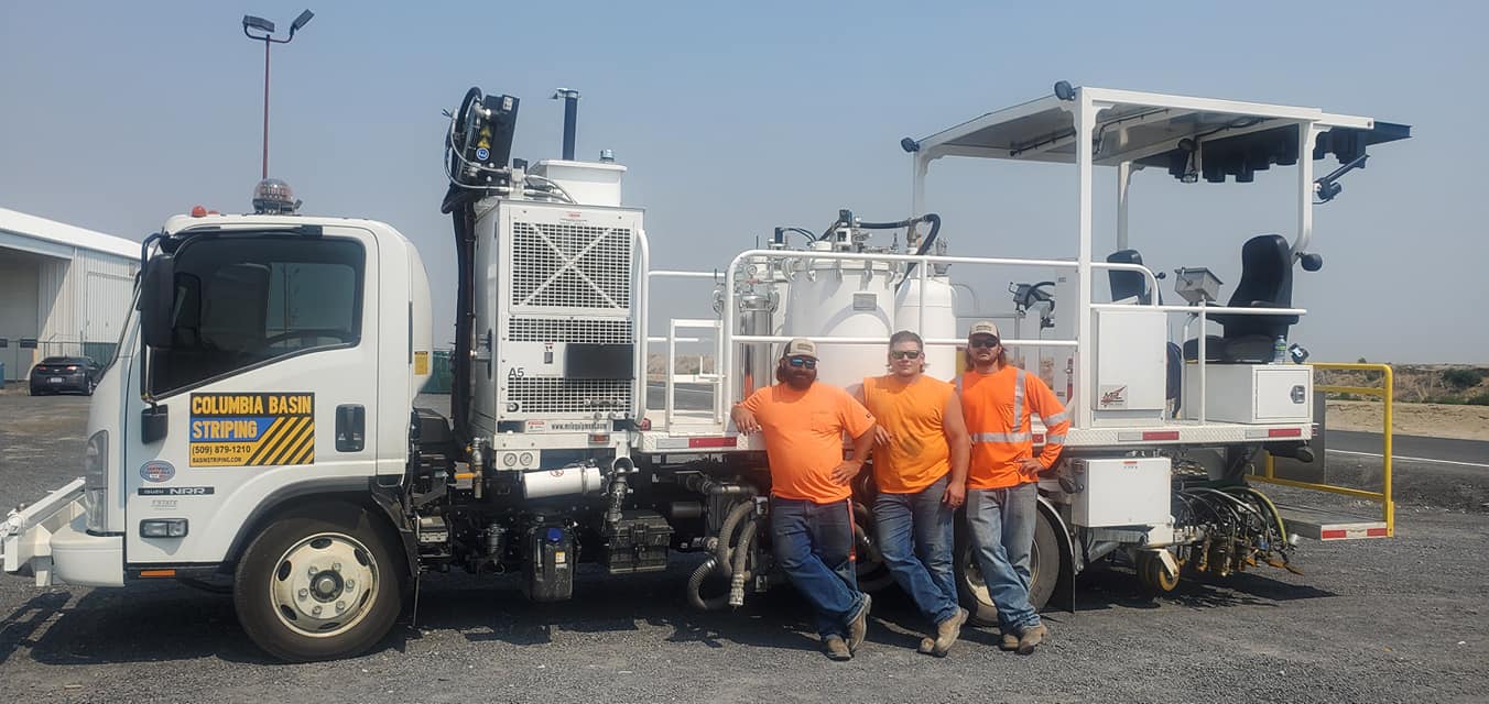 Three men in orange shirts standing next to a truck.