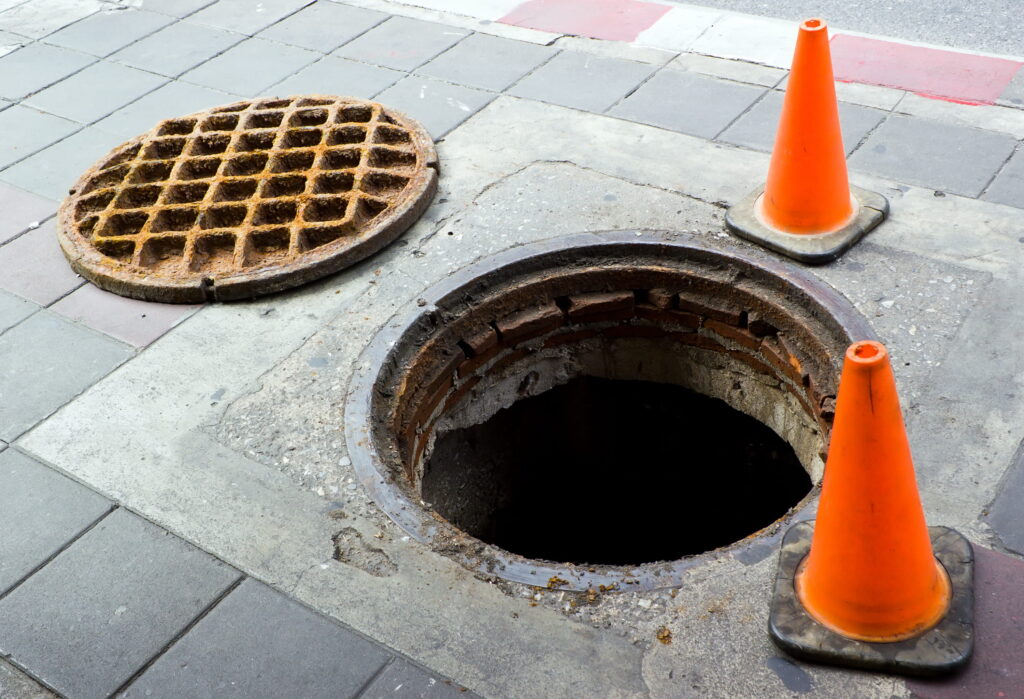 Open manhole with traffic cones nearby.