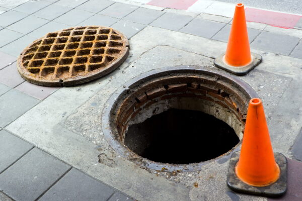 Open manhole with traffic cones nearby.